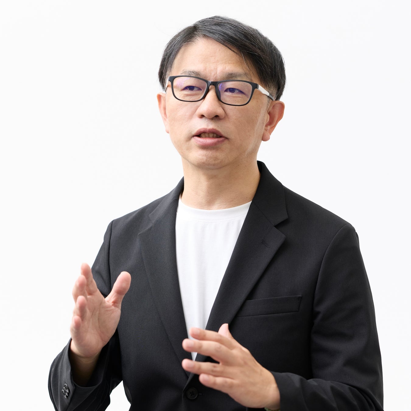 黒いジャケットと眼鏡を着用し身振りをつけて話している男性のバストアップ写真