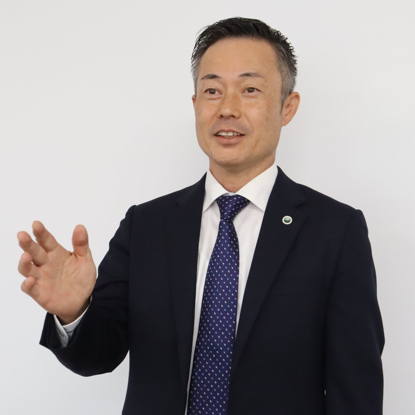 スーツとネクタイ姿で片手を前に出しながら話している男性のバストアップ写真