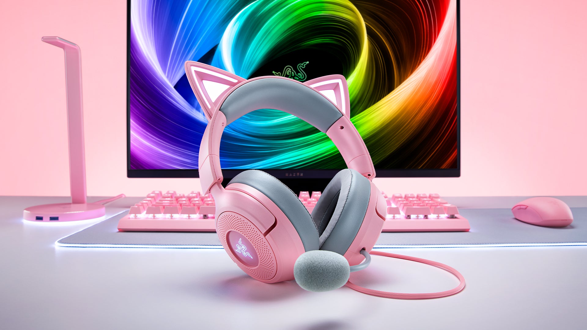 PCデスク上のキーボードやディスプレイの前に置かれたピンク色のネコミミ付きヘッドセットの写真。
