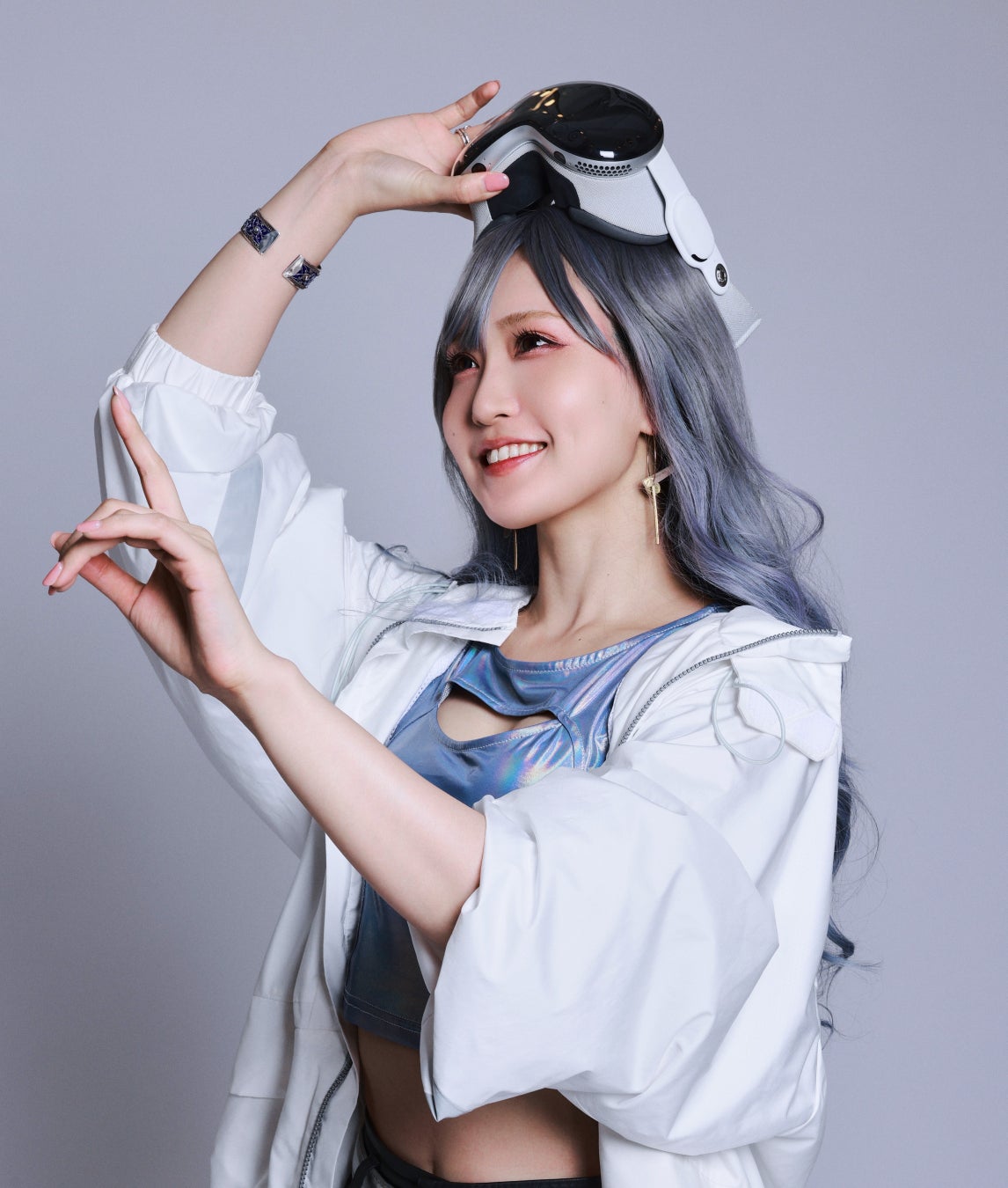 頭の上にヘッドセットを載せて笑顔を見せ、手元を掲げている人物のポートレート写真