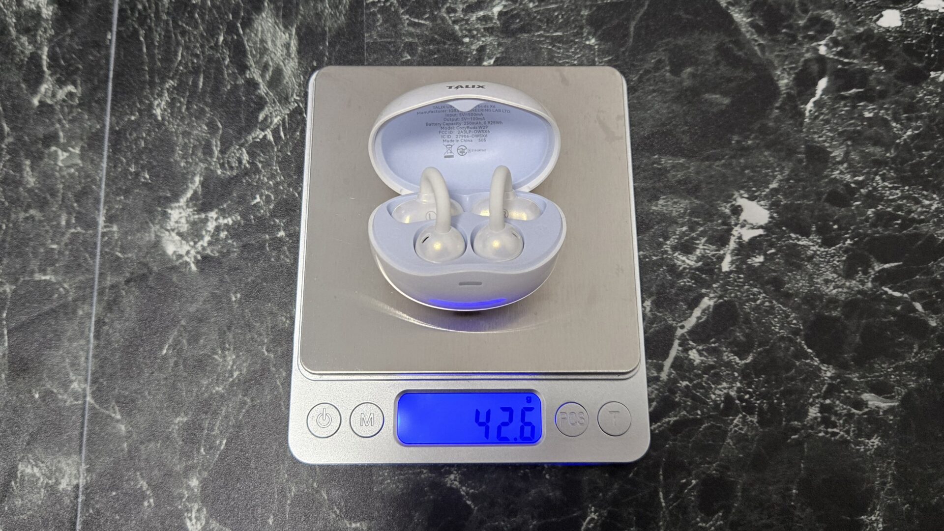デジタルスケールに載せられた白いワイヤレスイヤホンと充電ケースの重さが42.6グラムと表示されている