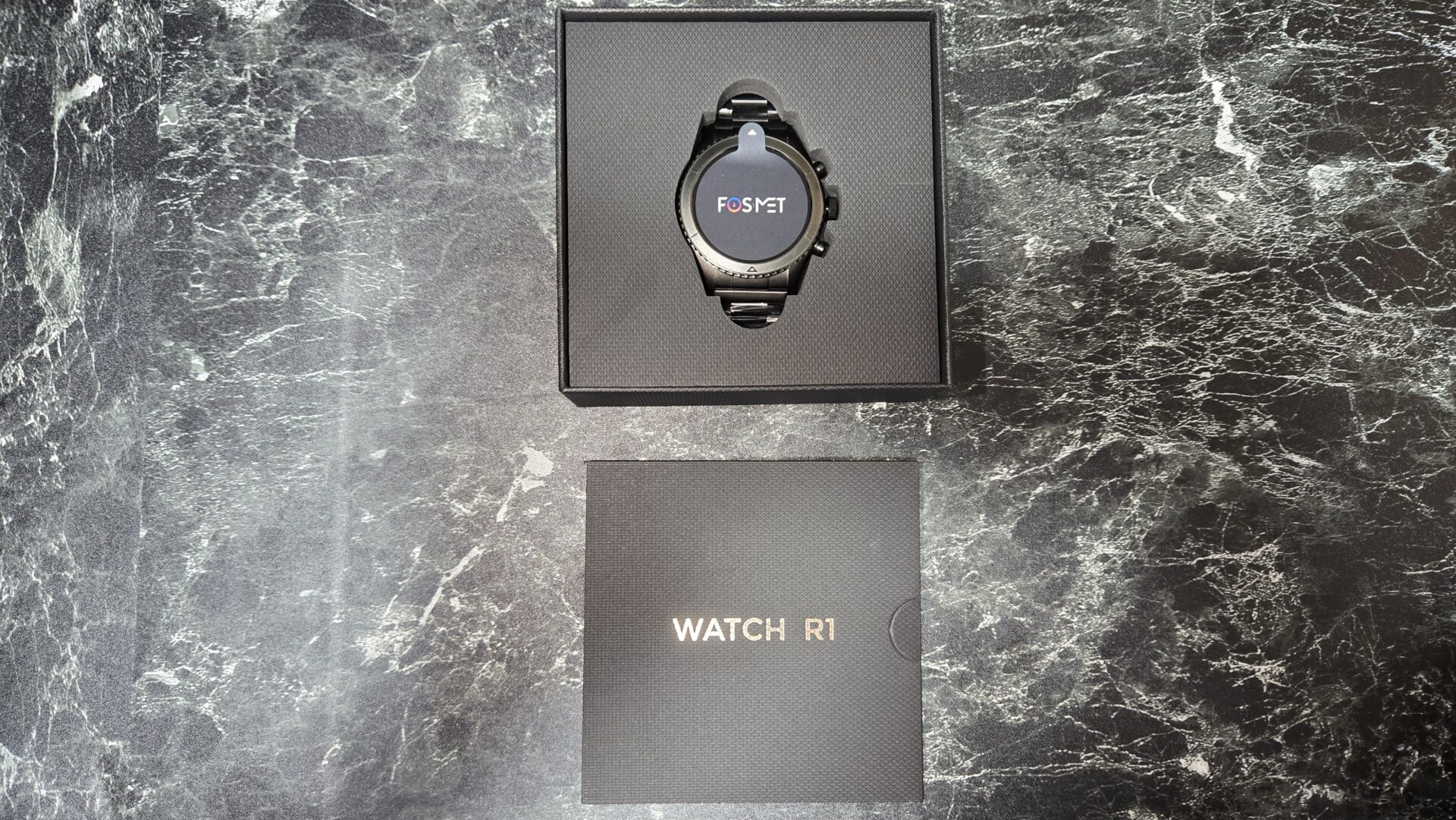 黒い大理石のテーブルに置かれたFOSYETスマートウォッチR1入りの箱とWATCH R1と書かれた箱