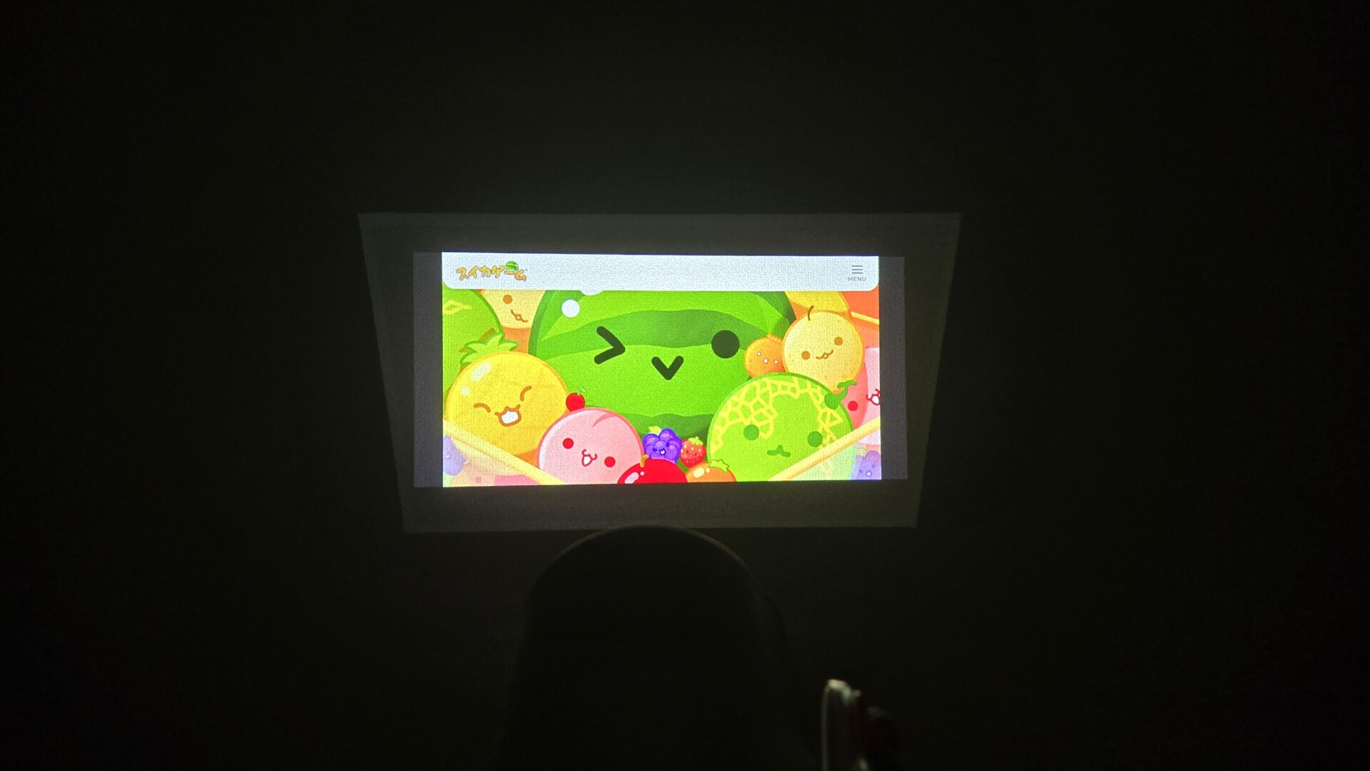 プロジェクターで壁に映し出されたスイカゲームの画面 中央の大きなスイカやレモンメロン桃など可愛い果物キャラクターが並ぶ