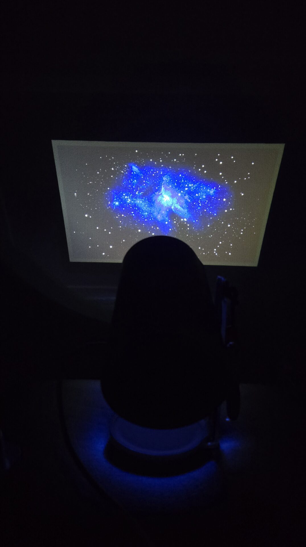 プラネタリウムで青い星雲と白い星が輝く宇宙が投影された暗い部屋