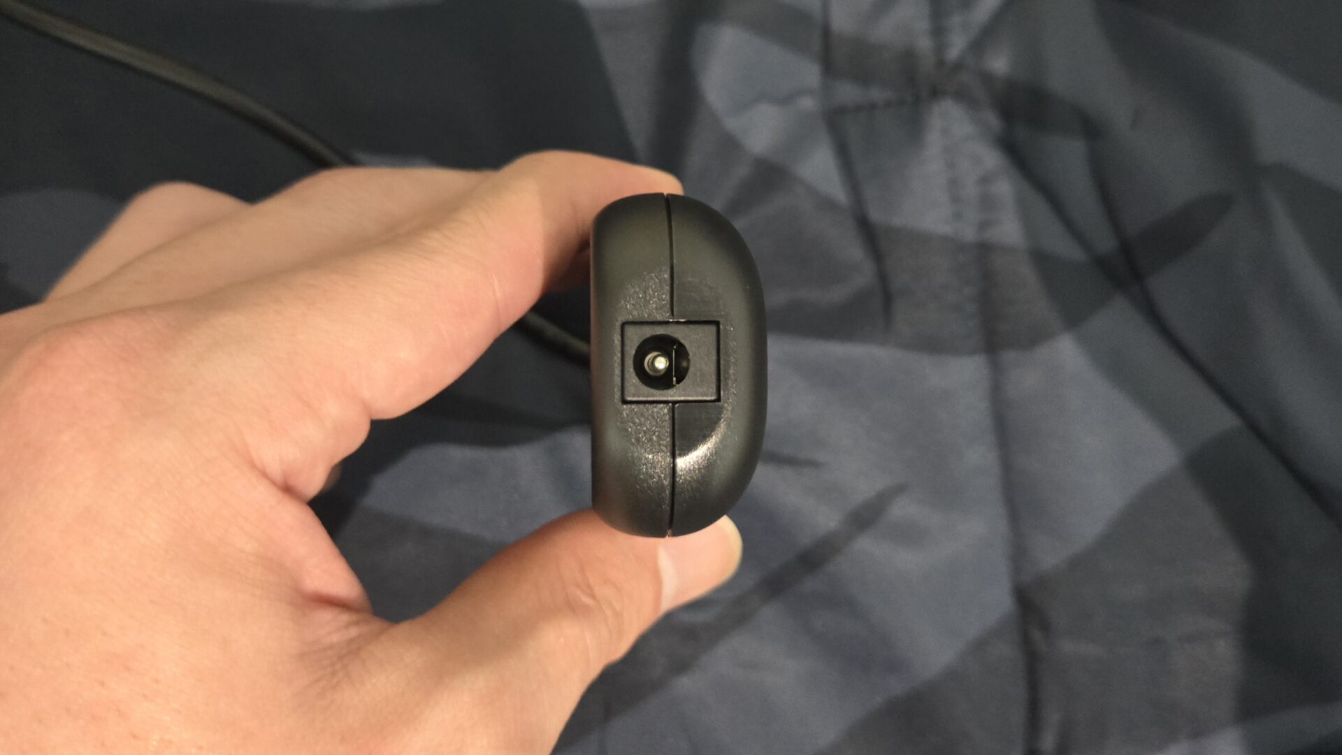 手で持っている黒い電子機器の丸い電源差込口