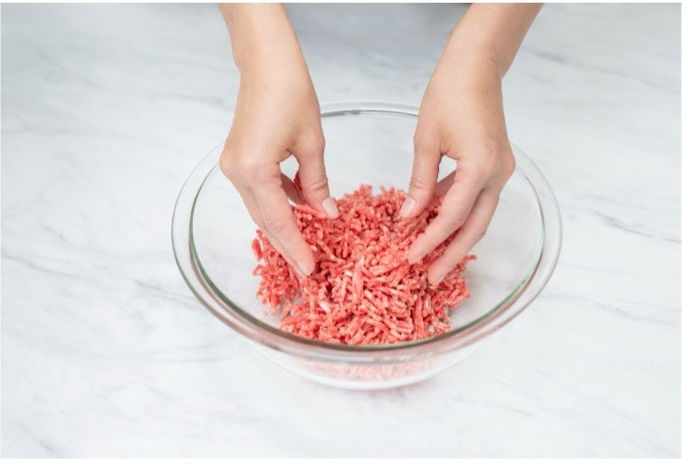 ガラスボウルの中でひき肉を手でほぐす様子