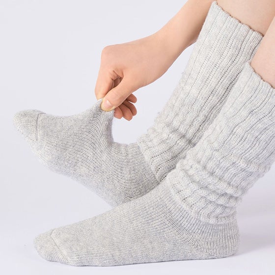 着用したグレーの靴下の甲部分を指でつまんで伸縮性を確認する様子