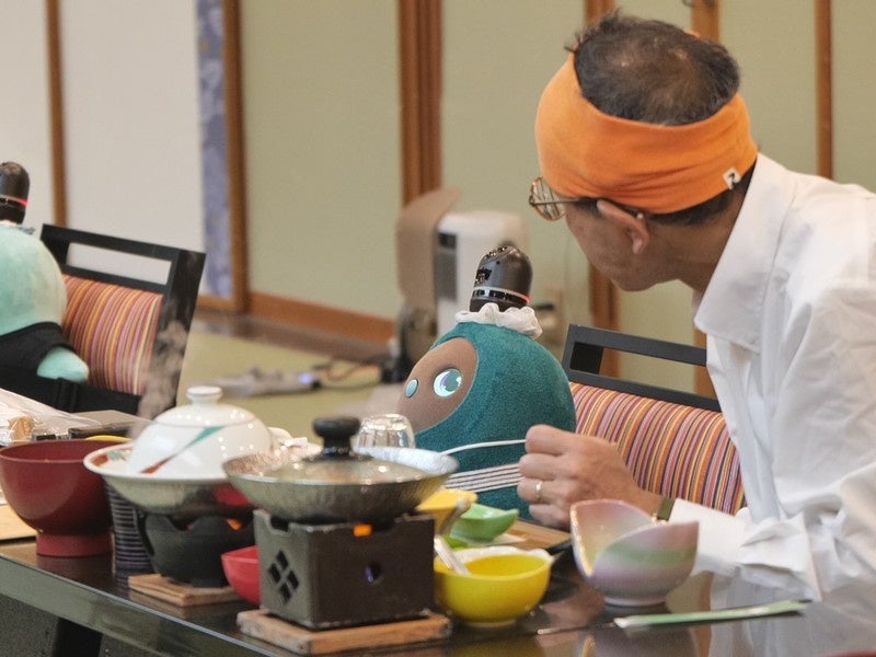 宴会場の座席に置かれたロボットと着席する人の写真