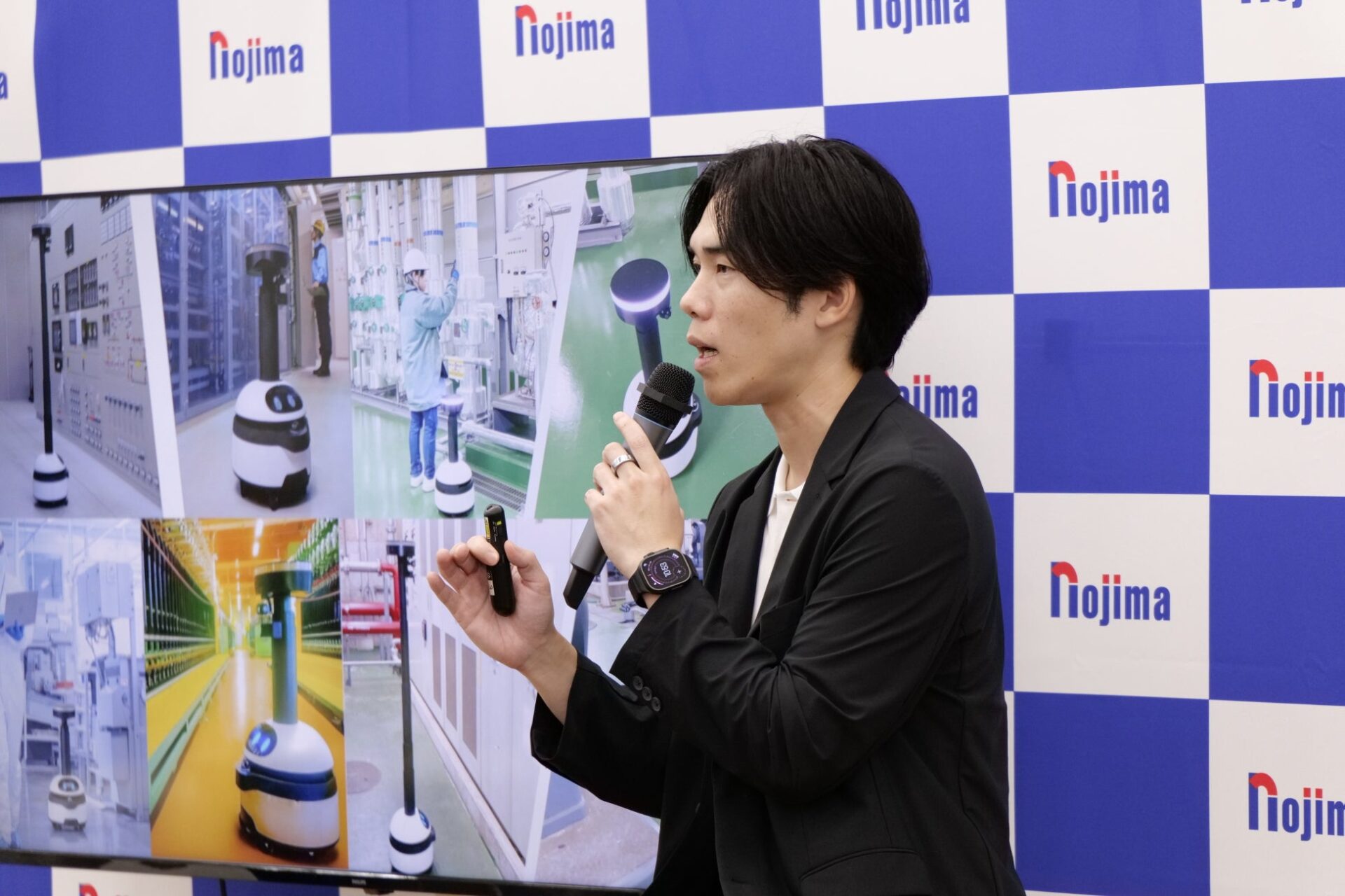 工場でのロボット稼働画像を映したスライド前で話す松井健氏の姿