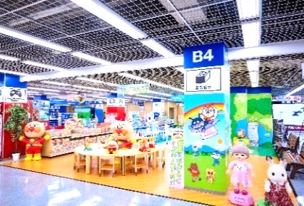 キャラクター人形や机が置かれたおもちゃ売り場の店内写真