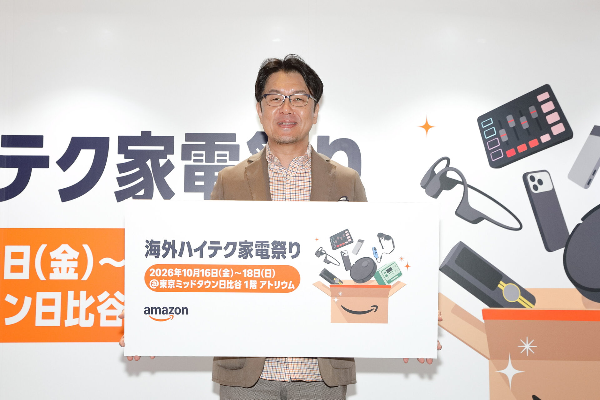 イベント名と会期が書かれたボードを掲げる登壇者の写真。背景には「海外ハイテク家電祭り」の装飾が広がっている