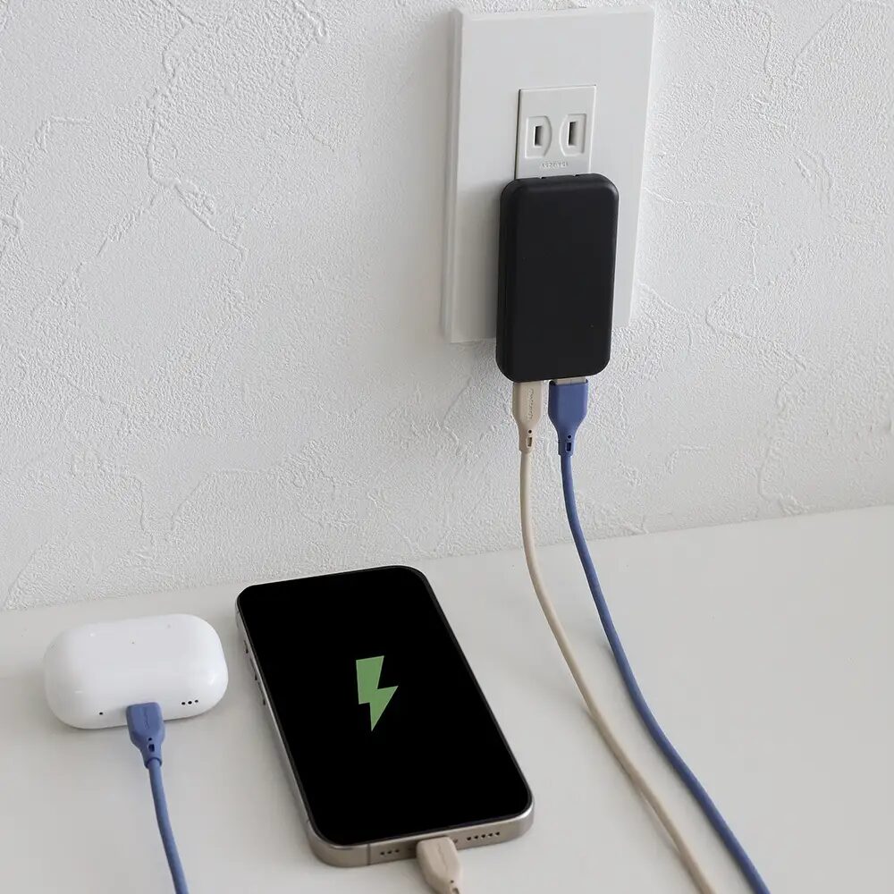壁のコンセントに挿した黒い充電器でスマートフォンと白いイヤホンケースを同時充電 スマートフォンの画面は緑の雷マーク表示
