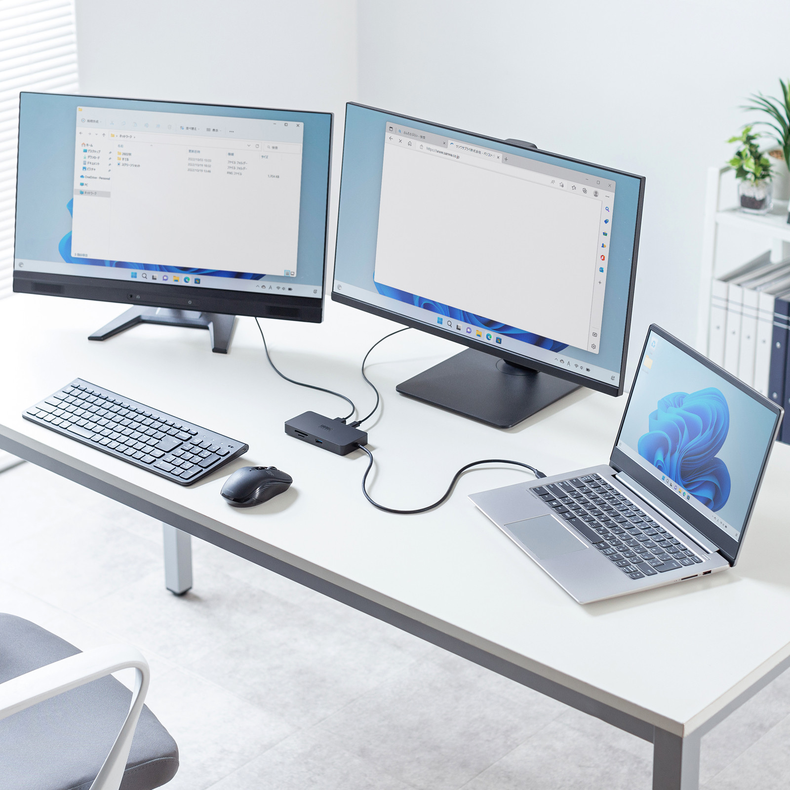 ノートパソコンとUSBハブそれに接続されたキーボードマウス2台のモニターがある白いデスクの仕事場