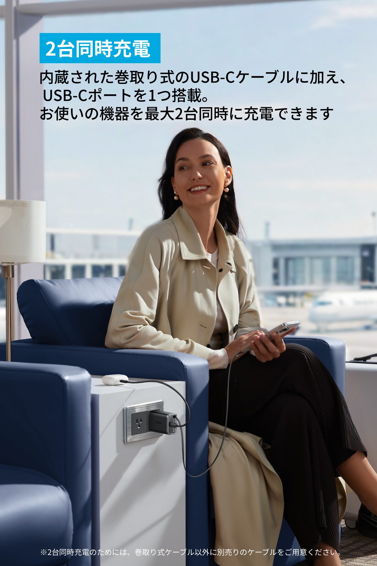 空港ラウンジで微笑む女性が巻取り式USB-CケーブルとUSB-Cポートを持つ充電器でスマートフォンを充電 2台同時充電